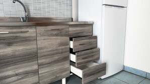 Una cocina con un lavamanos de acero inoxidable, un refrigerador blanco y muebles de madera con varios cajones.