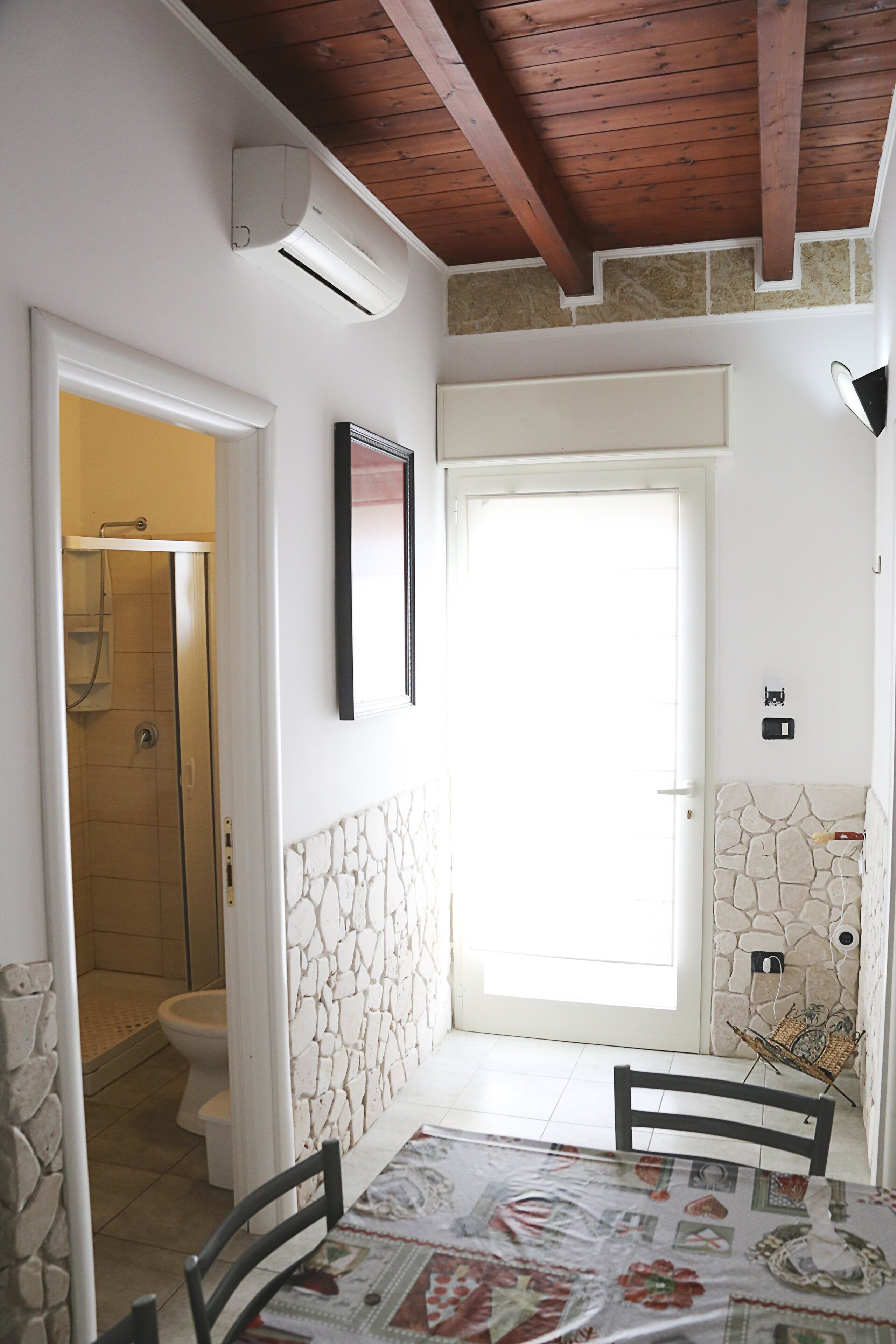 Une salle de bain avec douche, toilettes et une porte donnant sur un coin repas équipé d’une table et de chaises.