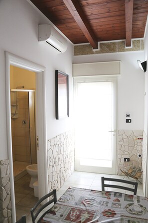 Ein Badezimmer mit Dusche, Toilette und einer Tür zu einem Essbereich mit Tisch und Stühlen.