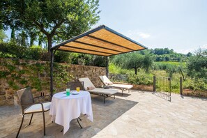 An outdoor patio with a table and chairs, a pergola, and a view of a vineyard. - The Club House (Castelnuovo Berardenga)