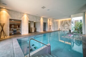 Una piscina interior moderna con agua cristalina, una barrera de vidrio y una pared de piedra.