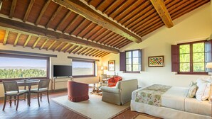 Un salón amplio con techo de madera, un ventanal con vistas al paisaje, un televisor y una zona de estar acogedora.