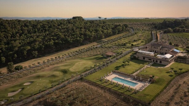 Vista aérea de una propiedad con un edificio grande, una piscina y amplios jardines, incluyendo un campo de golf y viñedos.