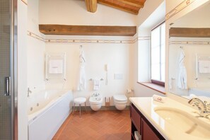 A bathroom with a bathtub, two toilets, a sink, and a large mirror. - The Club House (Castelnuovo Berardenga)