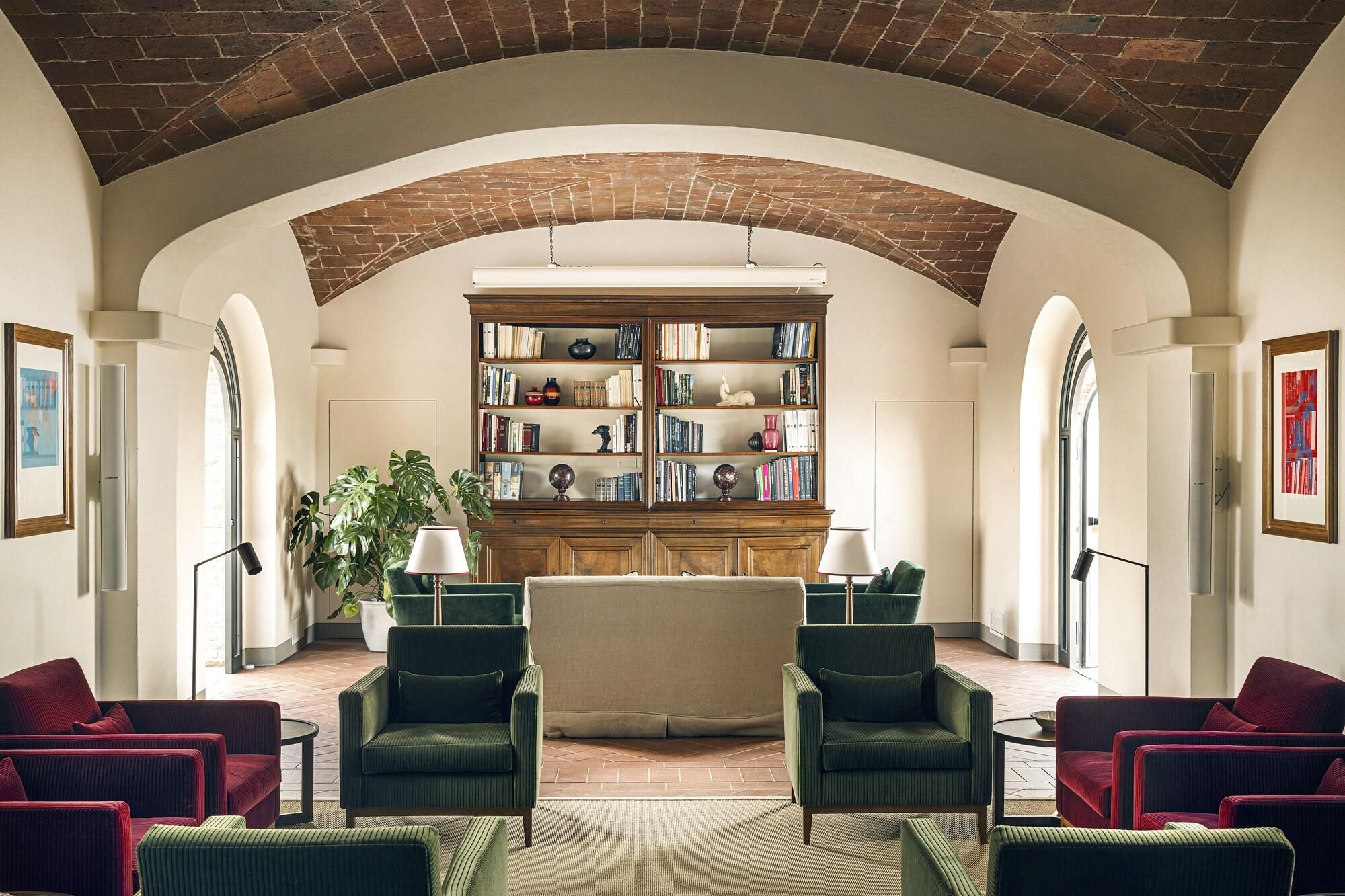 A library with bookshelves, two green armchairs, a beige sofa, and a red armchair.