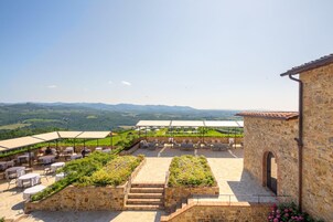 Un patio al aire libre con paredes de piedra, mesas y sillas, con vistas a un paisaje pintoresco.