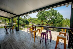 An outdoor patio with wooden flooring, tables, and colorful stools. - Sleepover Kruger Gate (Mbombela)
