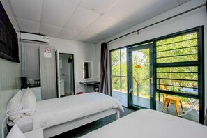 A hotel room with two beds, a bathroom, a TV, and a large window with a view of greenery. - Sleepover Kruger Gate (Mbombela)