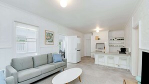 A modern living room with a grey sofa, a white coffee table, and a kitchen area with white cabinets and a bar counter.