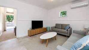 A modern living room with a flat-screen TV, two sofas, a coffee table, and a door leading outside.