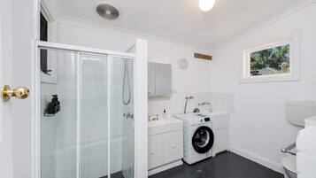 A modern bathroom with a glass shower enclosure, a washing machine, and a toilet.
