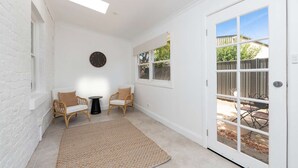 A bright, white-walled room with a large sliding glass door leading to a backyard. There are two wicker chairs and a small round table.
