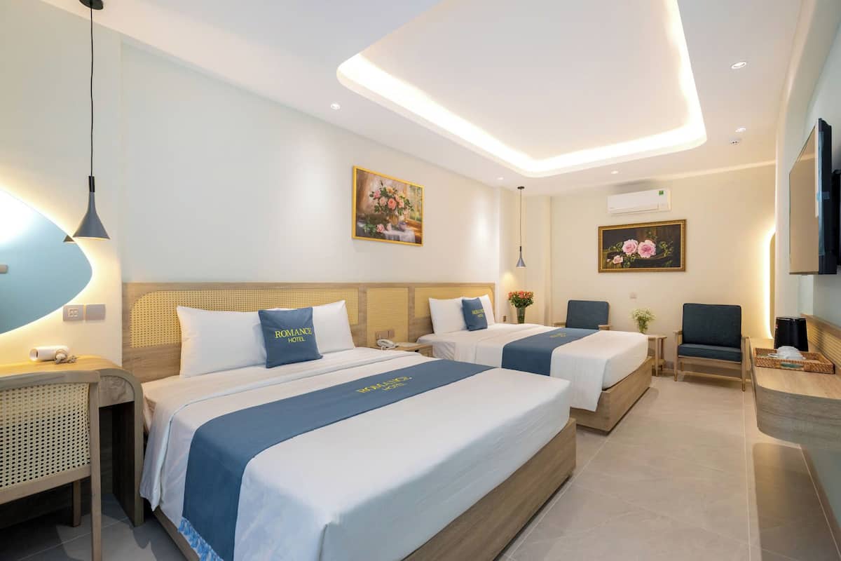 Habitación de hotel con dos camas, un escritorio, una silla, televisión y obras de arte en las paredes.