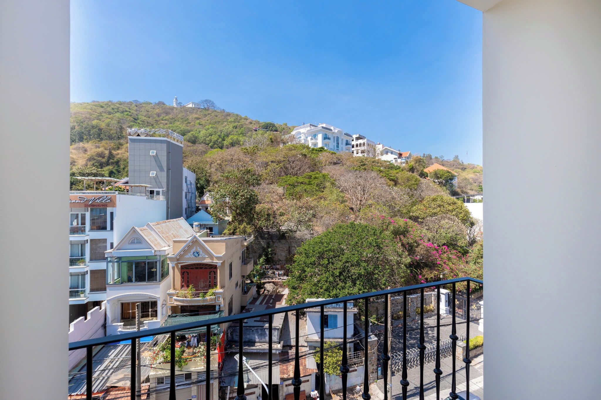 A residential area with buildings on a hillside, a balcony with a railing, and a clear blue sky.