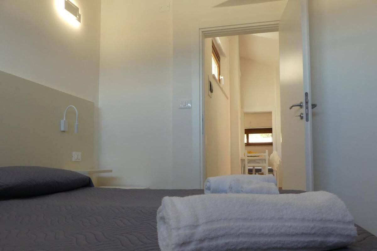 A hotel room with a bed, a bedside table, a wall-mounted light, and a door leading to a bathroom.