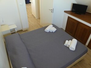 Ein kleines, ordentlich bezogenes Bett mit grauen Betttextilien und zusammengerollten Handtüchern.
