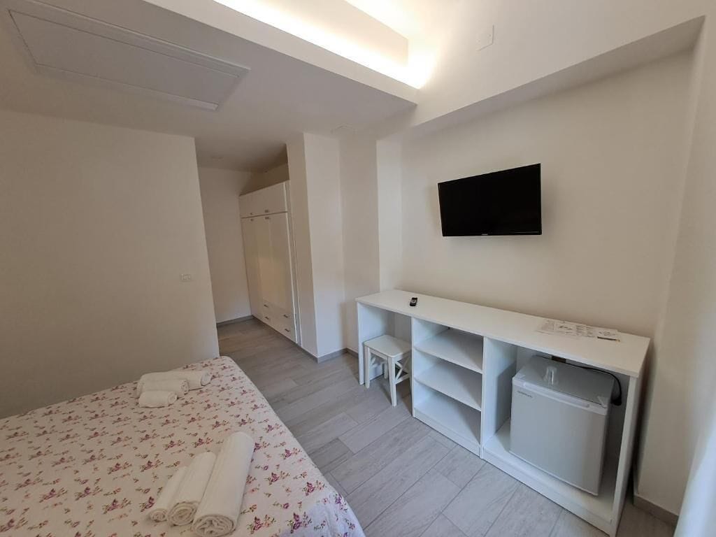 A modern hotel room with a bed, a TV mounted on the wall, a small desk, and a washing machine.