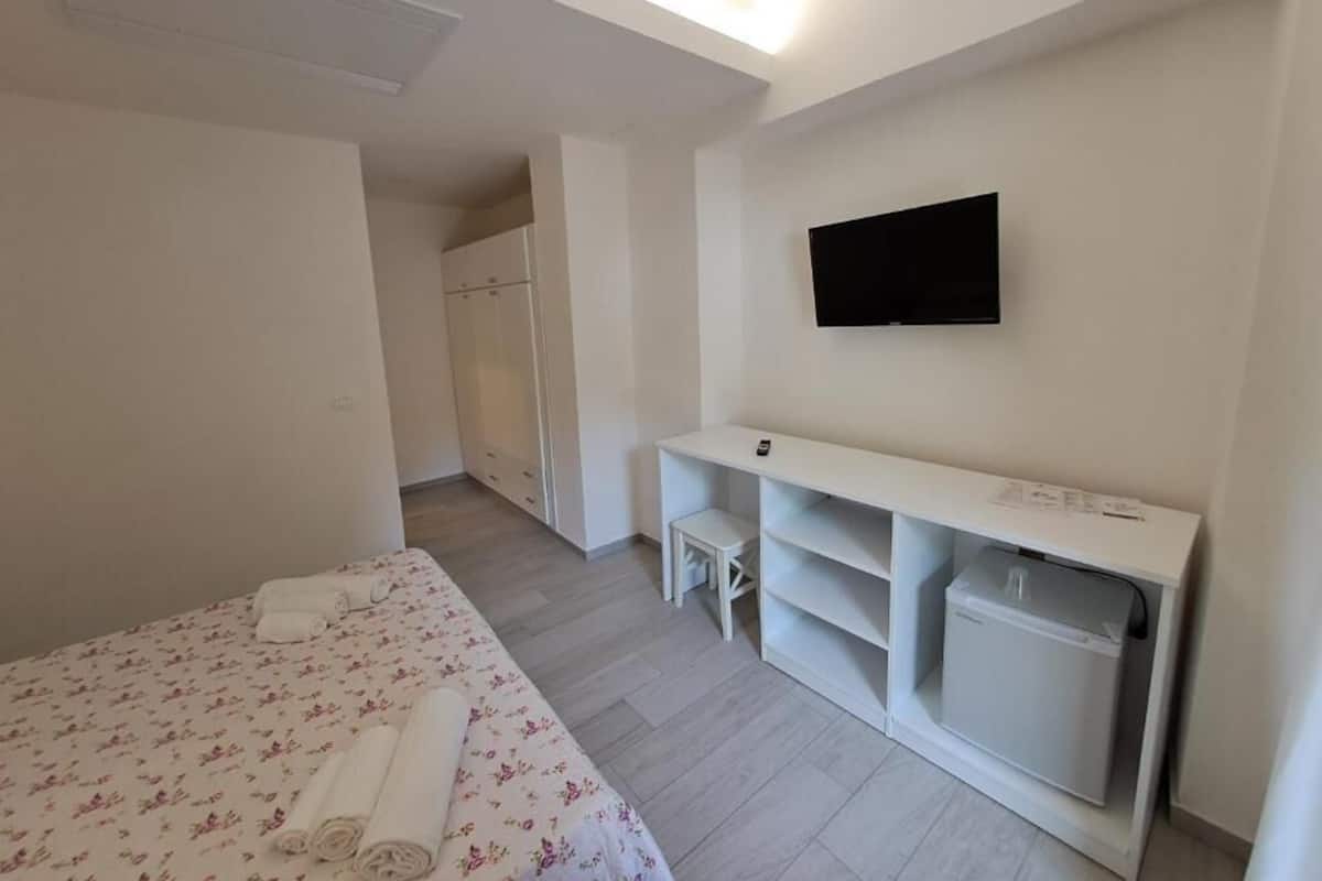 A modern hotel room with a bed, a TV mounted on the wall, a small desk, and a washing machine.