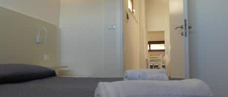 A hotel room with a bed, a bedside table, a wall-mounted light, and a door leading to a bathroom.