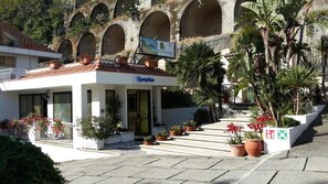 A reception area with a sign, potted plants, and a staircase leading to an upper level. - Le Roccette Mare Beach Hotel & Restaurant (Tropea)