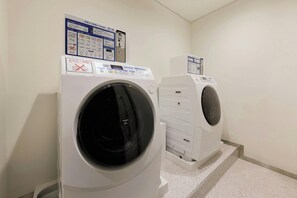 A laundry room with two front-loading washing machines and a dryer, with instructional signs above them. - Hotel Unizo Kyoto Karasuma Oike (Kyoto)