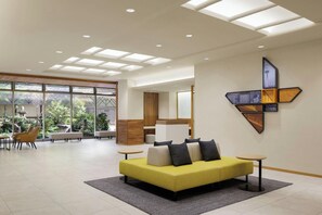 A modern hotel lobby with a yellow sofa, a dining area, and a large window with a view of greenery. - Hotel Unizo Kyoto Karasuma Oike (Kyoto)