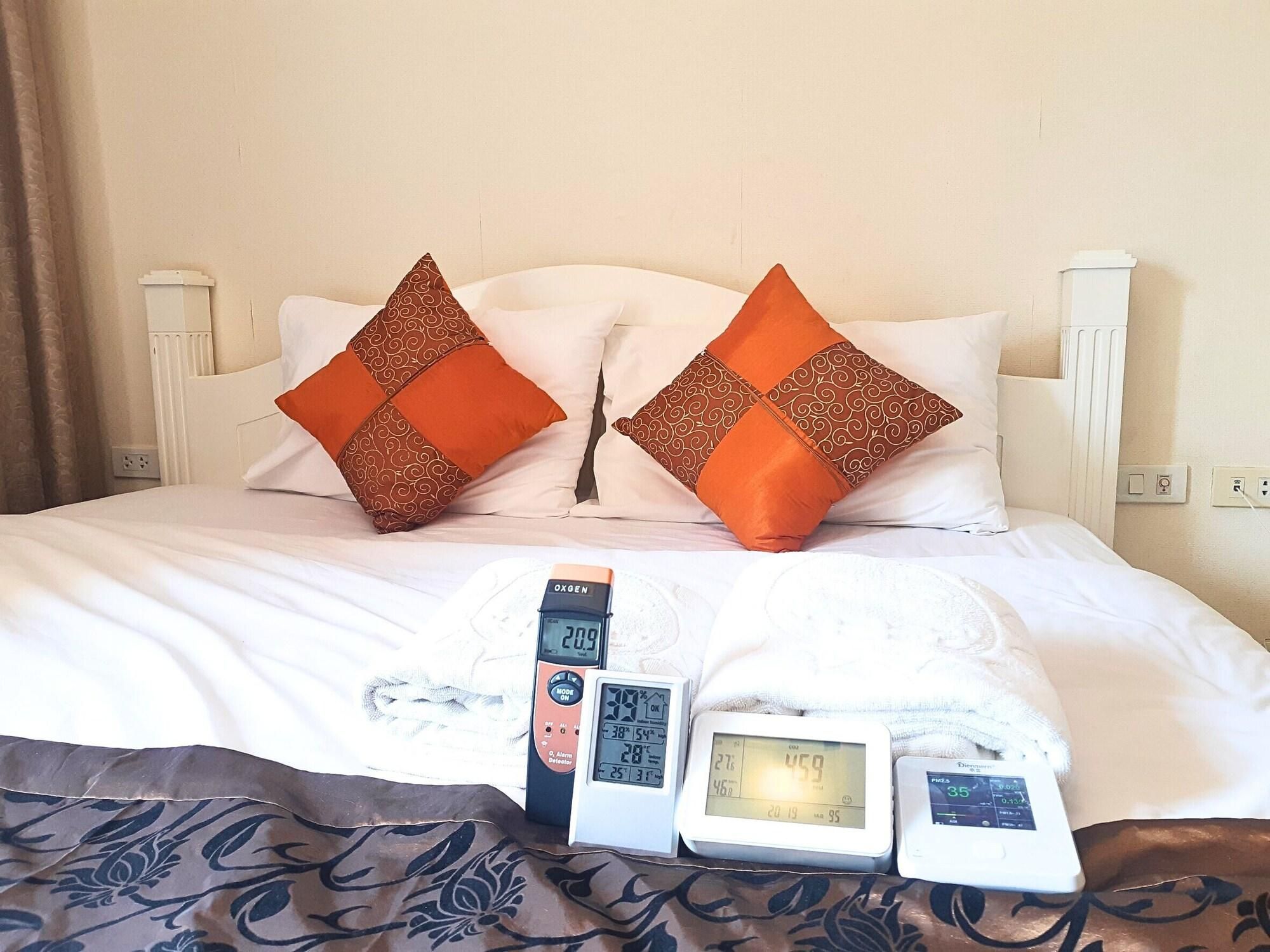 Una cama con dos almohadas naranjas, un cabecero blanco y tres relojes digitales que muestran la hora y la temperatura.