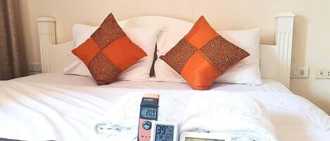 Una cama con dos almohadas naranjas, un cabecero blanco y tres relojes digitales que muestran la hora y la temperatura.