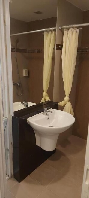A bathroom with a white sink, a mirror, a shower, and a towel rack. - Grandsmile Welnez Condo Pattaya (Pattaya)