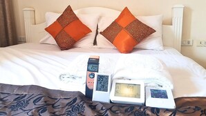 Ein Bett mit zwei orangefarbenen Kissen, einem weißen Kopfteil und drei digitalen Uhren, die Zeit und Temperatur anzeigen.