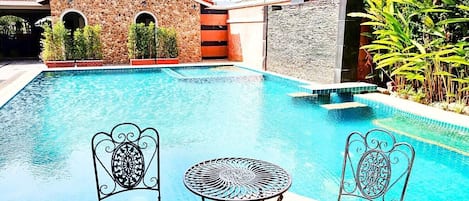 A swimming pool with two ornate metal chairs and a small table.