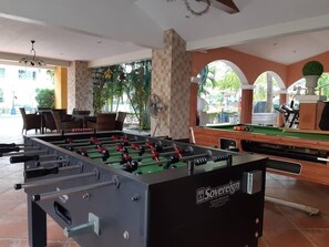 A foosball table labeled 'Sovereign' in a room with a pool table, seating area, and large windows overlooking a green outdoor area. - Grandsmile Welnez Condo Pattaya (Pattaya)