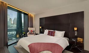 Ein modernes Hotelzimmer mit einem großen Bett, einem Sessel, einem Schreibtisch und Blick auf die Stadt.