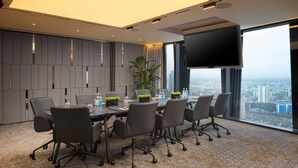 Ein moderner Konferenzraum mit einem großen Tisch, Stühlen, einer Pflanze und Blick auf die Stadt durch große Fenster.