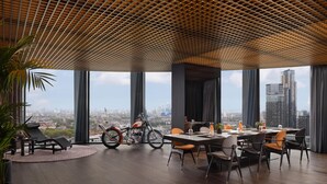 Ein moderner Essbereich mit großem Tisch und Stühlen, einem Motorrad und Blick auf die Stadt durch große Fenster.