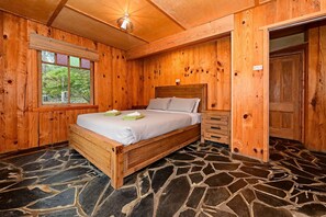 Une pièce en bois avec un lit, un sol en pierre et une fenêtre équipée de stores.