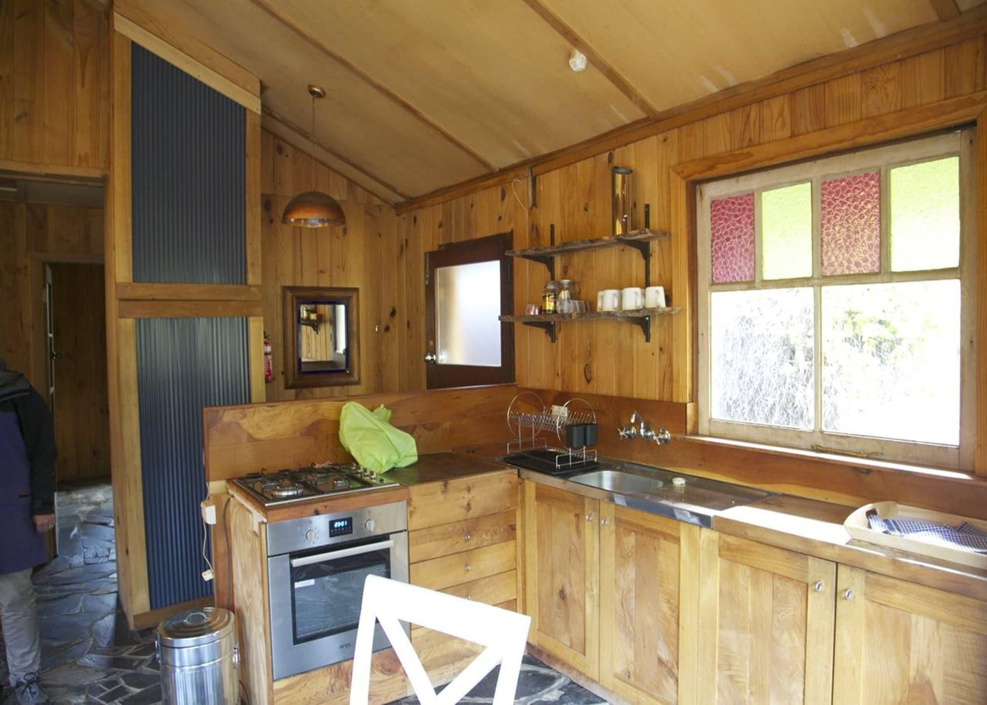 Cocina de cabaña de madera con estufa, horno, lavaplatos y ventana con vidrio emplomado.