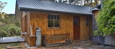 A rustic cabin with a metal roof, wooden walls, and a stone-paved entrance.