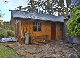 Una cabaña rústica con techo de metal, paredes de madera y un acceso empedrado.
