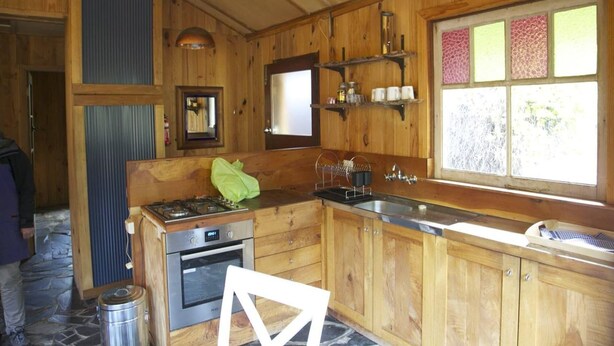 Eine Holzhütte mit einer Küche, inklusive Herd, Backofen, Spüle und einem Fenster mit Strukturglas.
