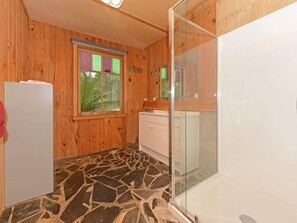 Une salle de bain avec un sol en pierre, des murs en bois, une douche en verre et un lavabo blanc.