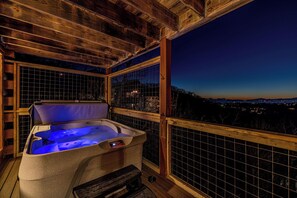 Un bain à remous doté d’un panneau de commande, entouré de rampes en bois et offrant une vue sur le paysage urbain au crépuscule.