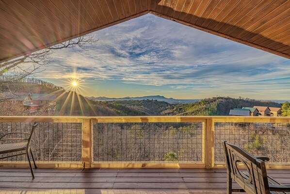 Une terrasse en bois offrant une vue sur un paysage montagneux, avec une balustrade en bois et un banc.