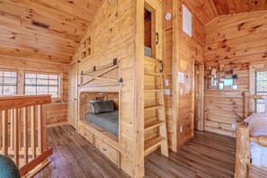 Une cabane en bois avec un lit superposé, une terrasse en bois et une fenêtre équipée de stores.