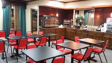 A restaurant with red chairs and black tables, a counter with a coffee machine, and a brick wall.