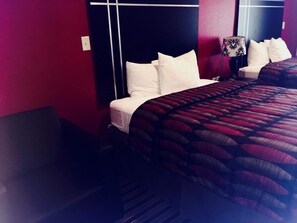 A hotel room with a bed, white pillows, a patterned bedspread, and a nightstand with a lamp. - Texan Inn And Suites Tilden (Tilden)