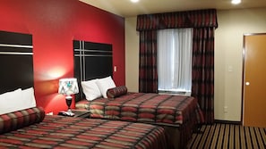 A hotel room with two beds, a nightstand, a lamp, and a window with curtains.