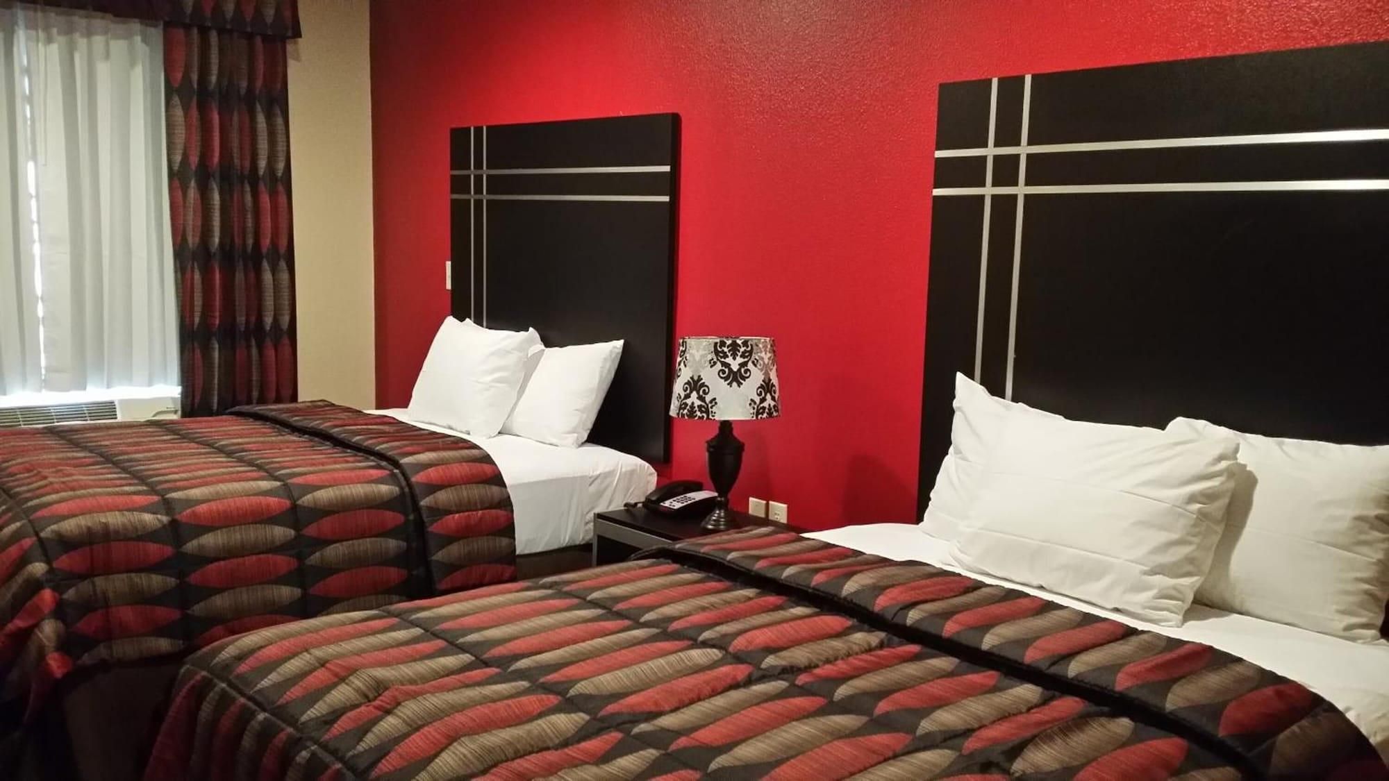 A hotel room with two beds, each with a patterned bedspread and white pillows. There is a nightstand with a lamp between the beds.