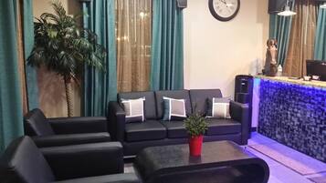 A modern living room with a black sofa, a coffee table, and a reception desk with a blue-lit counter.
