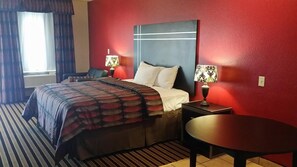 A hotel room with a bed, two bedside tables with lamps, a round table, and a window with curtains. - Texan Inn And Suites Tilden (Tilden)